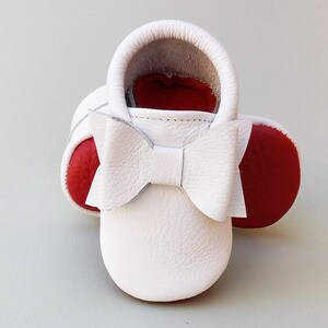 Puede incluir: Mocasines de beb&eacute; de cuero blanco con suelas rojas y un lazo blanco. Los zapatos de suela blanda est&aacute;n dise&ntilde;ados para beb&eacute;s y ni&ntilde;os peque&ntilde;os. Los zapatos miden aproximadamente 10 cm de largo.