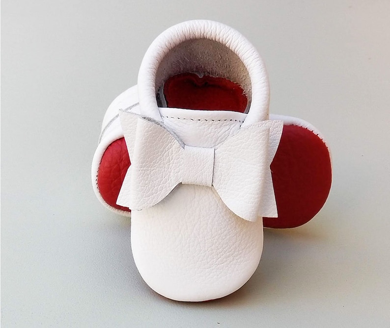 Puede incluir: Mocasines de beb&eacute; de cuero blanco con suelas rojas y un lazo blanco. Los zapatos de suela blanda est&aacute;n dise&ntilde;ados para beb&eacute;s y ni&ntilde;os peque&ntilde;os. Los zapatos miden aproximadamente 10 cm de largo.