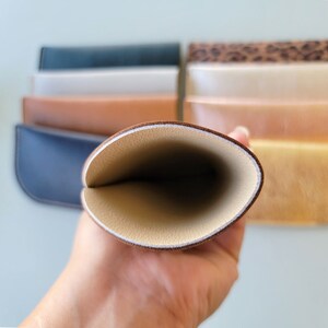 May include: A brown leather glasses case with a cream colored interior. The case is open and the interior is visible.