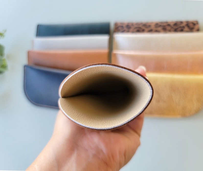 May include: A brown leather glasses case with a cream colored interior. The case is open and the interior is visible.