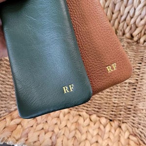 May include: Two leather phone cases, one in forest green and the other in brown, are displayed. Both cases have the initials "RF" in gold lettering. The cases have a textured surface.