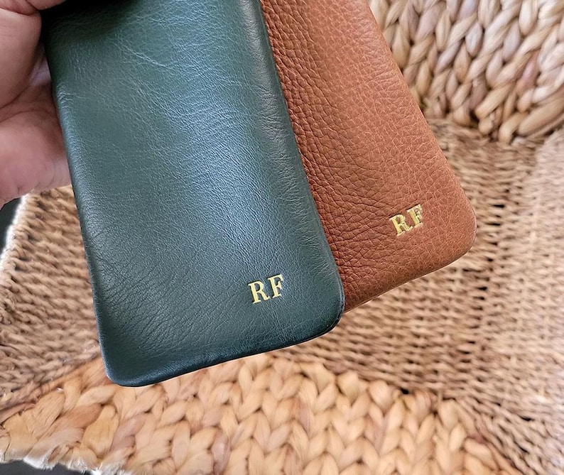 May include: Two leather phone cases, one in forest green and the other in brown, are displayed. Both cases have the initials "RF" in gold lettering. The cases have a textured surface.