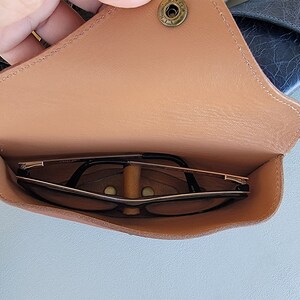 以下が含まれることがあります： スナップ留め具と中の眼鏡が付いた茶色の革製の眼鏡ケース