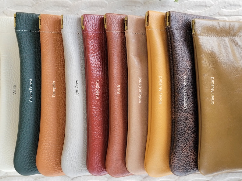May include: A collection of leather pouches in various colors, including white, green, orange, gray, red, brown, and tan. Each pouch has a stitched top and a brass-colored clasp. The colors are labeled with text.