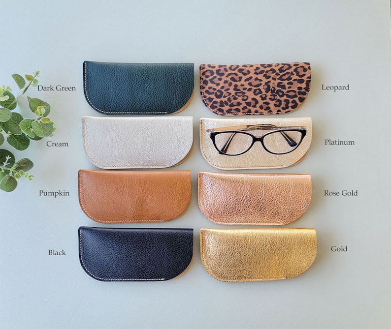 May include: Eight different colored leather eyeglass cases, including dark green, cream, pumpkin, black, leopard print, platinum, rose gold, and gold. The case in the middle row, second from the left, has a pair of eyeglasses inside.