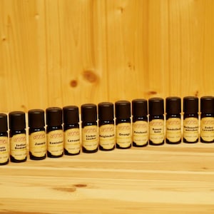Könnte beinhalten: Eine Reihe von 16 kleinen braunen Glasflaschen mit Etiketten, die verschiedene ätherische Öle enthalten, darunter Arabian Night, Gute Laune, Indian Summer, Jasmin, Kamille, Lavendel, Licher Räuber, Orange, Patchouli, Rosen Holz, Sandelholz, Walnüsse Marache, Zedern Lavendel und Zitrone.