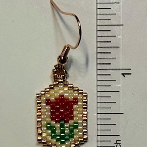 May include: A beaded earring with a rose design. The earring features a red rose with green leaves on a cream background, framed by gold beads. The earring is approximately 1 inch in length.
