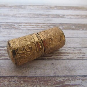 May include: A gold-coloured metal thimble with an intricate floral design. The thimble is closed and appears to be made of two pieces.