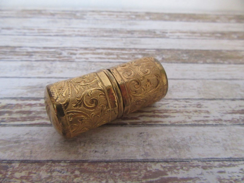 May include: A gold-coloured metal thimble with an intricate floral design. The thimble is closed and appears to be made of two pieces.