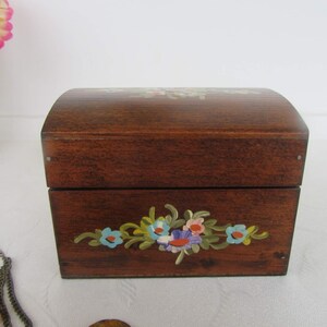 May include: A wooden box with a hinged lid, painted with a floral design in shades of blue, pink, green, and yellow. The box has a dark brown stain and is made of wood.