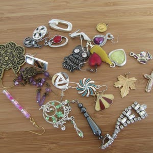 Könnte beinhalten: Eine Sammlung von silbernen und goldfarbenen Ohrringen, Anhängern und Charms. Die Ohrringe zeigen eine Vielzahl von Designs, darunter Blumen, Blätter und geometrische Formen. Die Anhänger und Charms umfassen ein Herz, ein Kreuz und eine kleine Eule.