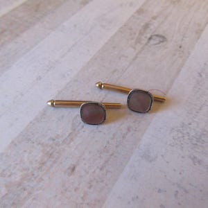 May include: A pair of gold cufflinks with a square, iridescent, pink stone set in a silver frame.