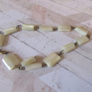 May include: A white, rectangular, beaded necklace with gold-toned metal connectors.