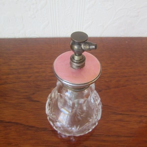May include: A clear glass perfume bottle with a pink and silver top and a decorative cut glass design.