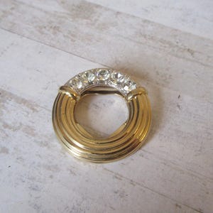 May include: A gold-toned ring with a circle design and clear rhinestones around the edge.