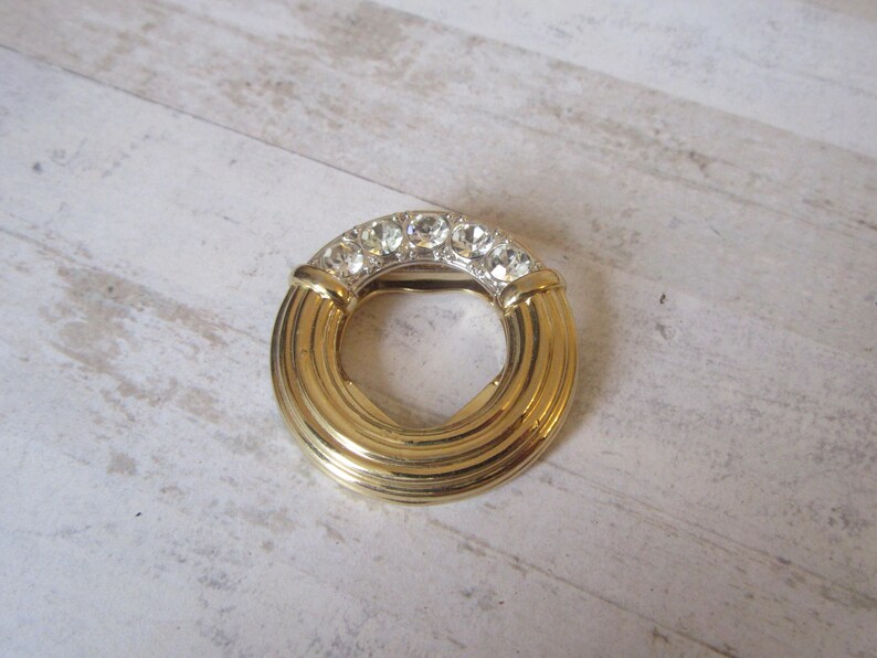 May include: A gold-toned ring with a circle design and clear rhinestones around the edge.