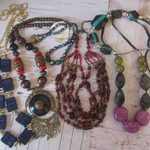 May include: Six different necklaces featuring a variety of beads and materials. The necklaces include blue, green, red, brown, and purple beads. Some necklaces have metal accents.