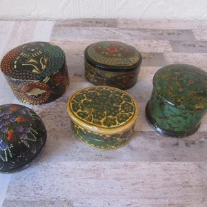 May include: Five small, round, hand-painted wooden boxes with intricate floral and animal designs. The boxes are in various shades of green, black, and yellow.