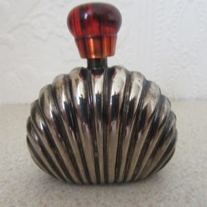 May include: A silver perfume bottle shaped like a seashell with a red plastic stopper.