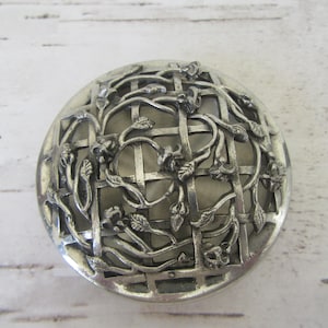 Könnte beinhalten: Silberner Blumentopf aus Metall mit Gitterdesign und filigranen Blumendetails.