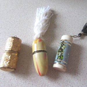 May include: Three vintage thimble cases. One is gold with an ornate design, one is white with a yellow and red design, and one is blue with a white and red design and the text "BONNI VILLA".