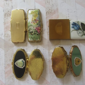 May include: Collection of vintage compacts in various shapes and designs. Includes rectangular and oval compacts with gold-tone metal cases. Some feature floral and landscape artwork, while others have textured surfaces or decorative accents.