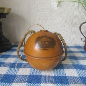 Könnte beinhalten: Eine runde, braune, dekorative Holzkiste mit einem Seilgriff. Die Kiste hat ein Schwarzweißbild eines Gebäudes auf der Vorderseite. Die Kiste steht auf einer blau-weiß karierten Oberfläche.