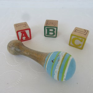 Könnte beinhalten: Holzbaufell mit den Buchstaben A, B und C. Ein Holzrassel mit blauen, grünen und weißen Streifen ist ebenfalls im Bild.