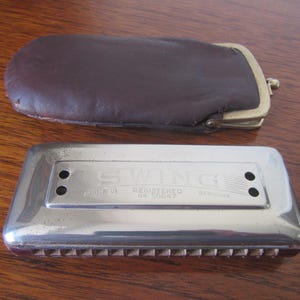 May include: A silver harmonica with a brown leather case. The harmonica is labeled "Swing Registered 48 50047 Germany".