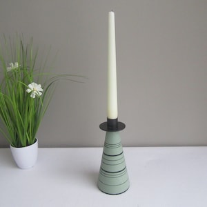 May include: A green and black candlestick with a tall white candle. The candlestick has a conical base with black stripes.