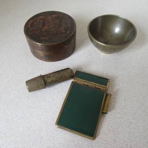 Può includere: Un set di quattro oggetti in ottone vintage: una scatola rotonda con un design inciso, una piccola ciotola con un design inciso, un ditale e una piccola scatola con cerniera verde e dorata.