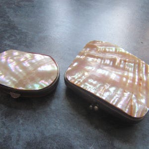 Puede incluir: Dos cajas antiguas de nácar. Una es ovalada, la otra rectangular con bordes redondeados. Ambas tienen superficies iridiscentes y nacaradas con un tono rosado cálido. Las cajas tienen marcos y bisagras de metal oscuro.