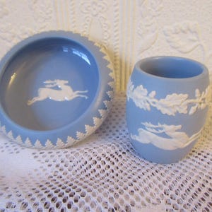 May include: A light blue ceramic bowl and small cup with white relief designs. The bowl features a running deer in the center and a decorative border. The cup has a similar design with a deer and foliage. Home decor.