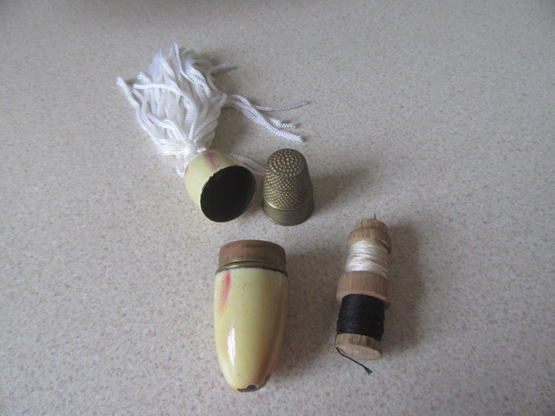 May include: A set of vintage sewing supplies including a thimble, a spool of thread, and a small needle case with a white tassel.