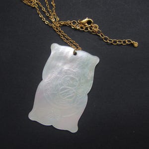 May include: A white mother of pearl pendant necklace with a gold chain. The pendant is shaped like two overlapping leaves with an intricate design.