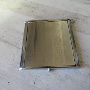 May include: A silver metal cigarette case with a geometric pattern.