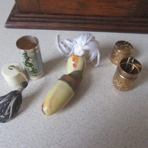 May include: A collection of vintage thimbles, including a white and gold thimble with a tassel, a white and gold thimble with a floral design, and two gold thimbles with intricate designs.