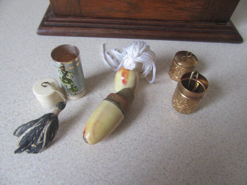 May include: A collection of vintage thimbles, including a white and gold thimble with a tassel, a white and gold thimble with a floral design, and two gold thimbles with intricate designs.