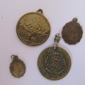 Könnte beinhalten: Vier antike goldfarbene Metallanhänger mit religiösen Motiven. Ein Anhänger zeigt einen Mann, der ein Kind trägt, ein anderer zeigt eine Frau mit einer Krone und ein weiterer zeigt arabische Schrift. Der vierte Anhänger ist ein rundes, verziertes Design.