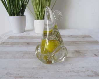 May include: A clear glass sculpture of a pear with yellow glass bubbles inside. The pear is sitting on a light wood surface.