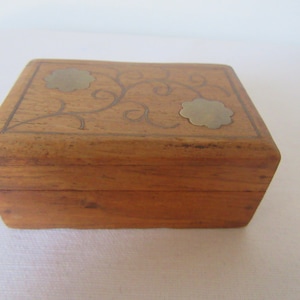 Könnte beinhalten: Eine kleine Holzkiste mit floralem Design und Messingakzenten. Die Kiste ist aus hellbraunem Holz gefertigt und hat einen Deckel mit Scharnier.