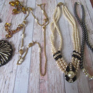 May include: Five necklaces with different styles and colours. One necklace has a large black and white pendant. Another necklace has a black and white pendant with a pearl in the centre. The other necklaces are made of pearls, gold beads, and black beads.