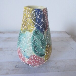 May include: A ceramic vase with a white, yellow, blue, green, and pink abstract pattern. The vase has a narrow neck and a wide base.