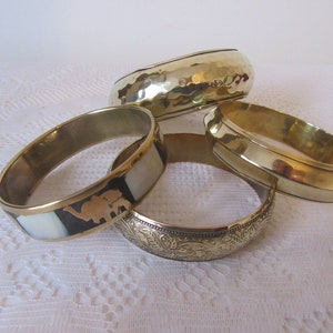 May include: Four gold-toned metal bangles. One bangle has a white and black inlay with an elephant design. Another bangle has an engraved floral pattern. The remaining two bangles are plain.