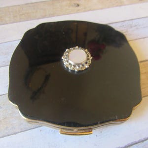 Portacipria vintage &quot;Melissa&quot;. Design in smalto nero e guilloché dorato. Cerchio in madreperla con bordo decorato color argento. Elegantemente sagomato e firmato.