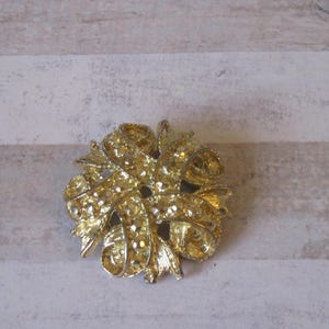 K&ouml;nnte beinhalten: Eine goldfarbene Brosche mit einem Design aus ineinander verschlungenen B&auml;ndern. Die Brosche ist filigran und detailliert, mit einer strukturierten Oberfl&auml;che.