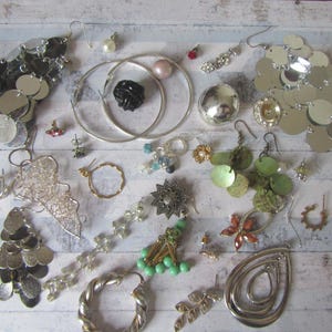 Könnte beinhalten: Eine Sammlung von silbernen und goldfarbenen Ohrringen, darunter Creolen, Ohrhänger und Ohrstecker. Einige Ohrringe sind mit Pailletten, Perlen und anderen dekorativen Elementen verziert.