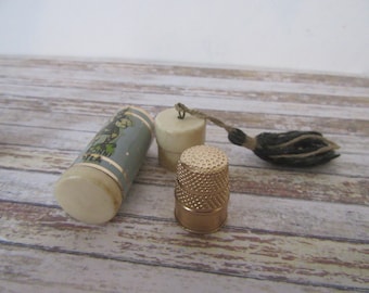 May include: A vintage sewing kit with a white and blue cylindrical case with a cartoon image and text that reads "RONNI FILA", a white thimble with a gold top, and a black and brown tassel.