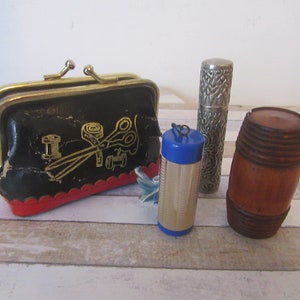 Puede incluir: Un conjunto de cuatro artículos de costura vintage, que incluye una cartera de monedas de cuero negro con bordados dorados de herramientas de costura, un estuche para dedal de metal azul y plateado, un estuche para agujas de metal plateado y un soporte de carrete de madera.