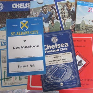 May include: A collection of vintage football programs and memorabilia. The items include programs for Chelsea Football Club, St. Albans City, and other teams. The programs feature team logos, match details, and stadium illustrations. The colors are primarily blue, red, and white.